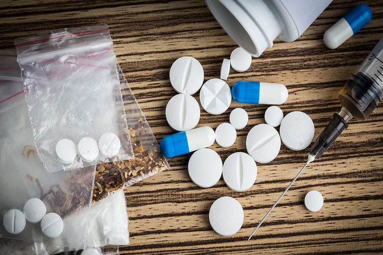 A collection of white tablets, blue capsules, a syringe, and small plastic baggies on a wooden table, highlighting substance use issues addressed by Drug Rehab Fort Wayne Indiana.
