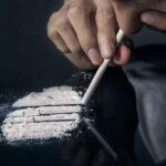 A person holding a rolled tube above lines of white powder on a dark surface, illustrating the health dangers of cocaine use in Fort Wayne.