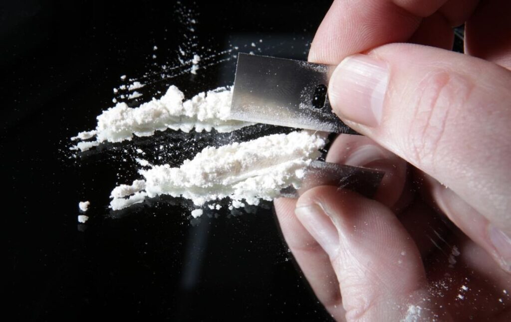 Close-up of hands using a razor blade to divide white powder into lines, representing the risks associated with cocaine use in Fort Wayne.