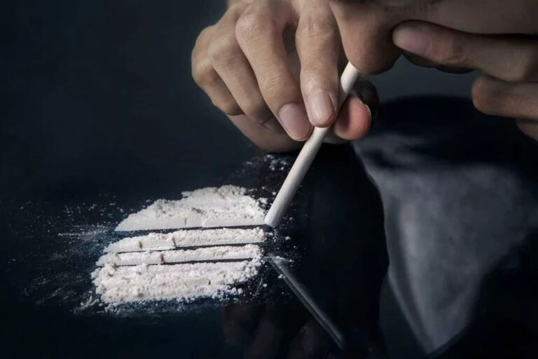A person holding a rolled tube above lines of white powder on a dark surface, illustrating the health dangers of cocaine use in Fort Wayne.