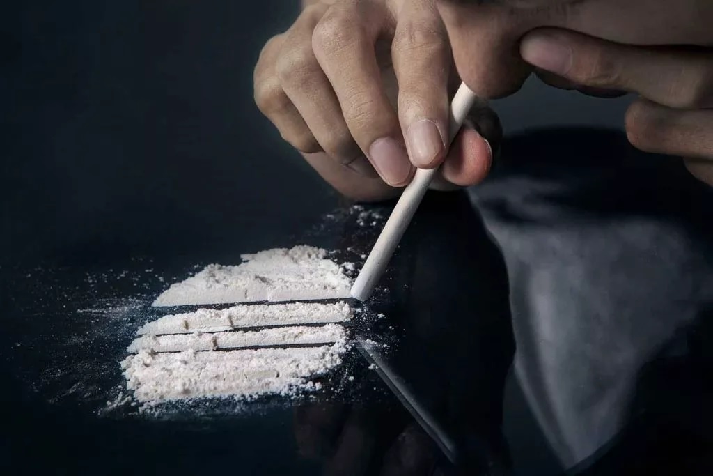 A person holding a rolled tube above lines of white powder on a dark surface, illustrating the health dangers of cocaine use in Fort Wayne.