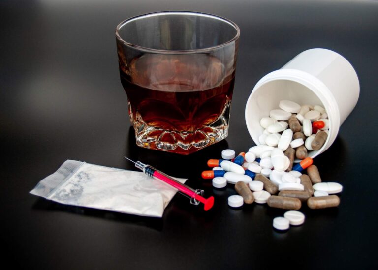 Spilled prescription pills, a glass of alcohol, and drug paraphernalia on a dark surface, highlighting the need for drug and alcohol rehab in Indianapolis.
