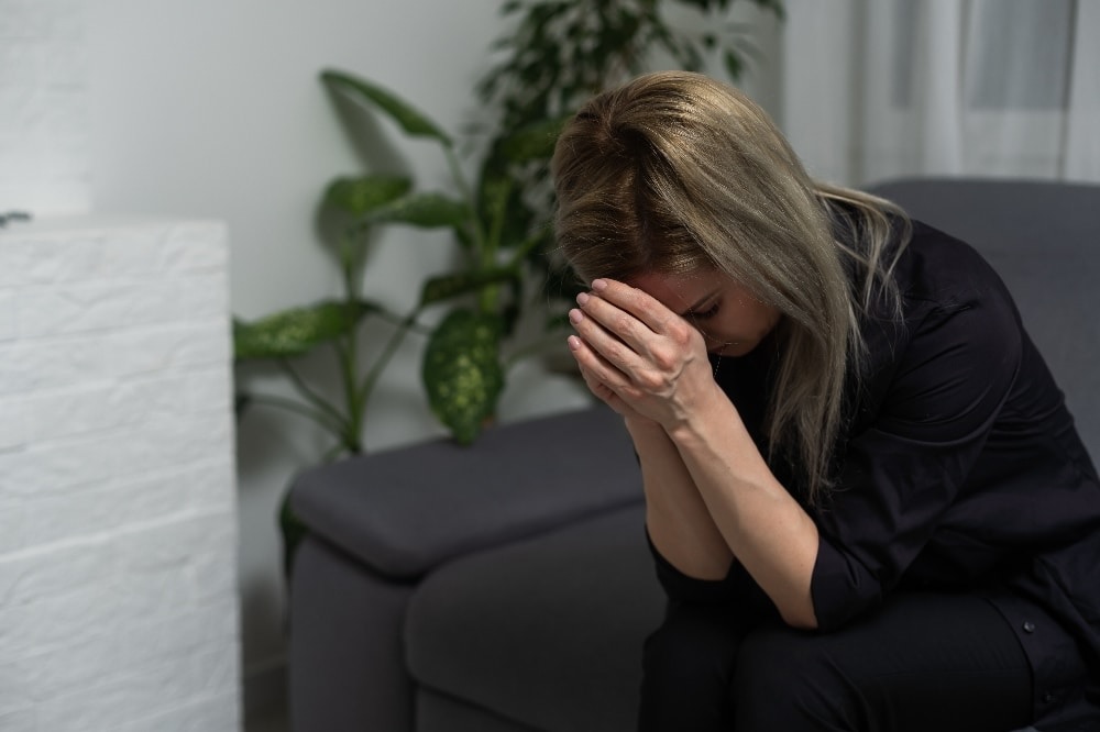A sad woman holding her face in her hands while coping with grief, showing the emotional challenges of maintaining sobriety after loss.