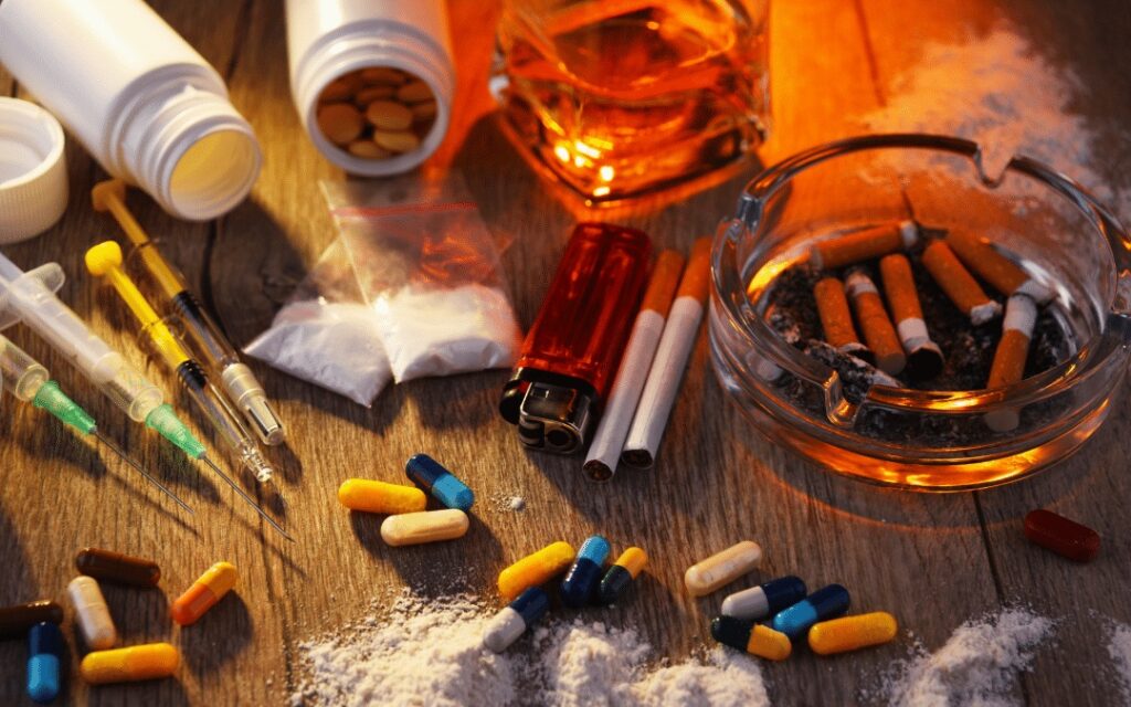 Various addictive substances and paraphernalia spread on a wooden table, emphasizing the challenges of navigating substance use treatment