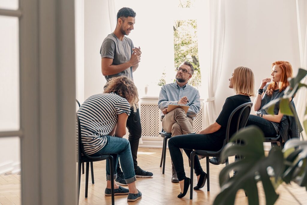 Diverse support group sitting in a circle listening to a man speak at a rehab center near me.