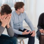 Therapist counseling a distressed man in a group session at a luxury addiction treatment center.