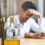 A stressed man surrounded by liquor bottles before entering a structured alcohol rehab program.