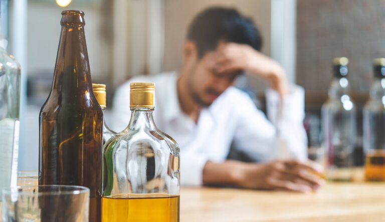 A stressed man surrounded by liquor bottles before entering a structured alcohol rehab program.