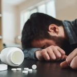 A person resting their head on a table next to alcohol and pills, illustrating the struggle before joining a confidential addiction treatment program.