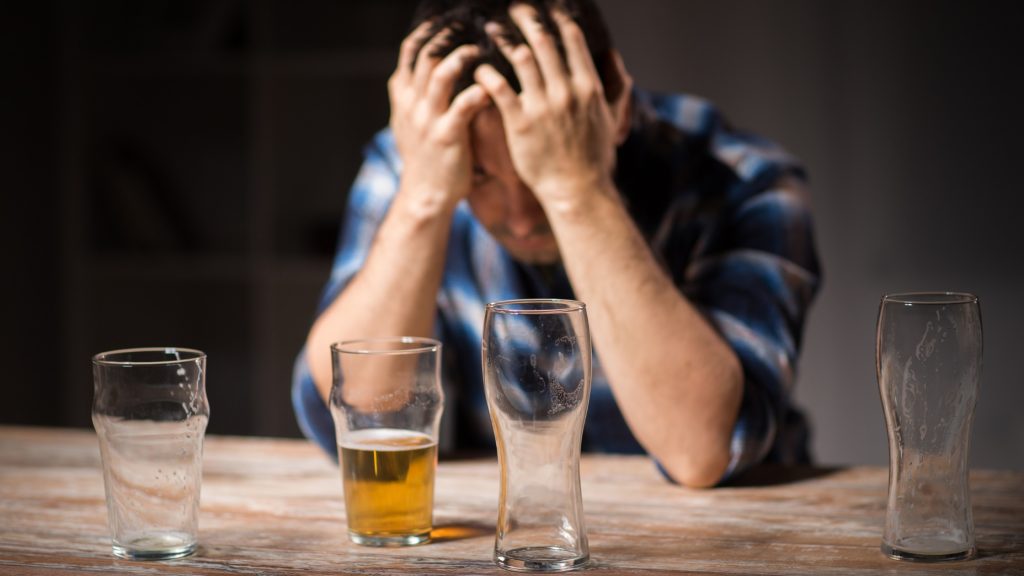 A distressed man holding his head in hands behind several empty beer glasses, highlighting the need for an alcohol withdrawal management program.