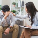 Compassionate counselor comforting a stressed man holding his head during a residential rehab transition session.