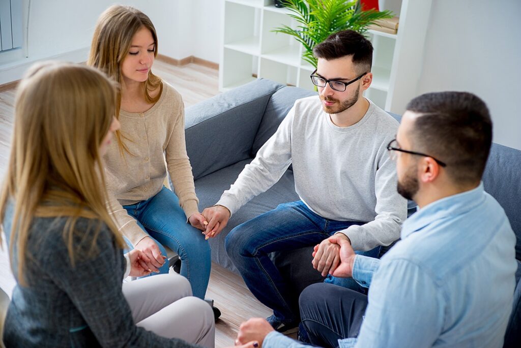 Group therapy participants sitting in a circle holding hands after learning how to verify insurance for rehab.